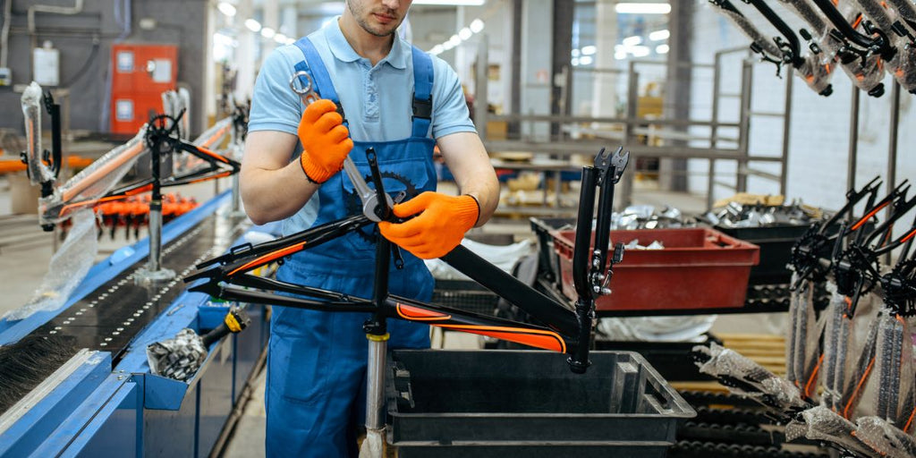 Staff in blue overalls and orange gloves installing gears on an e-bike frame at the DAMAXED factory.