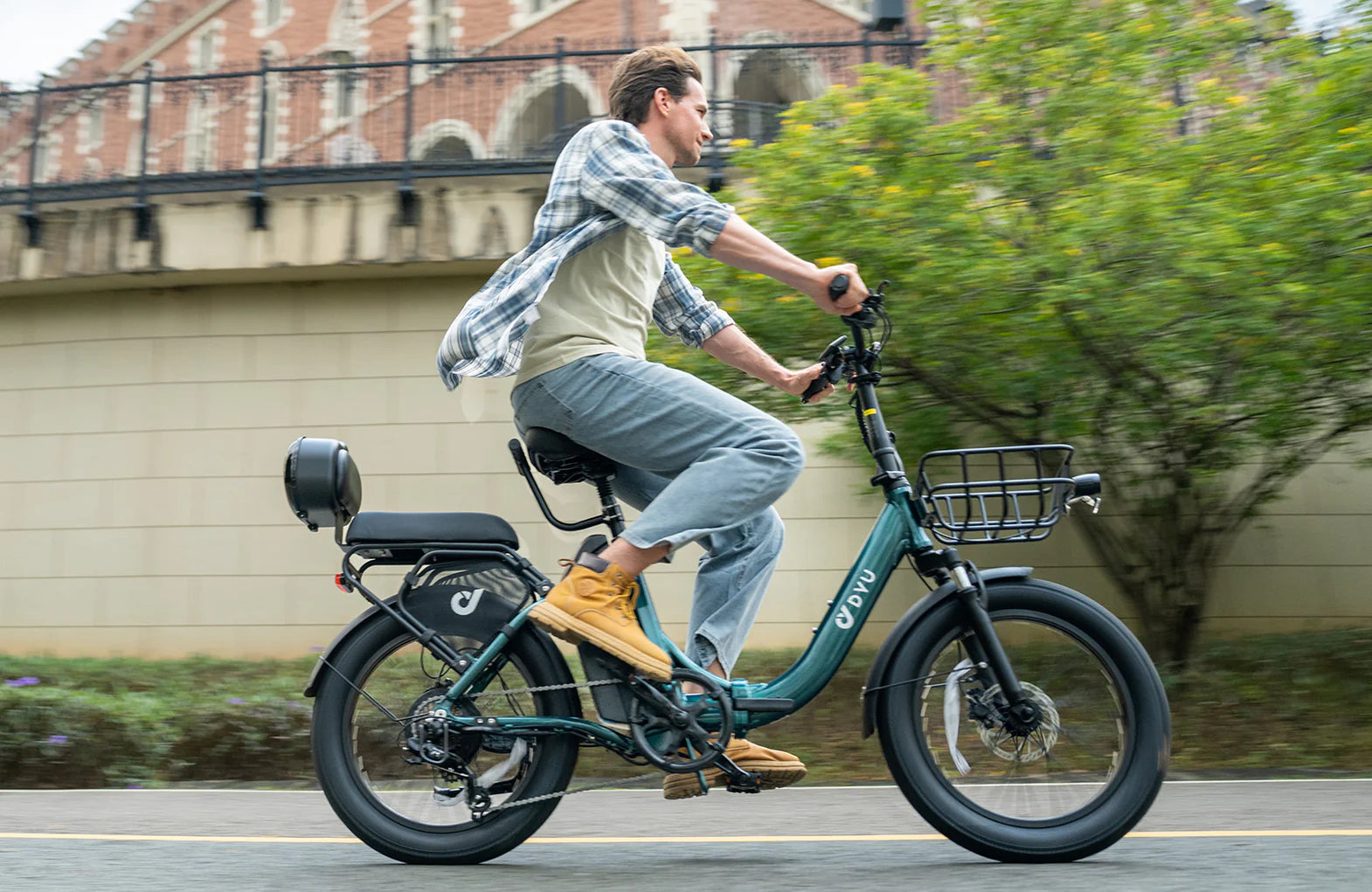 Man riding a DYU C9 electric bike on a city street with a building and tree in the background