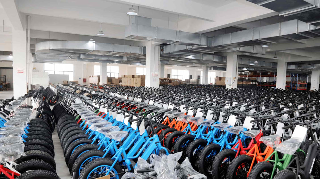 Neatly arranged DAMAXED warehouse workshop displays quality-checked electric fat tire bikes in green, blue, orange, and red 