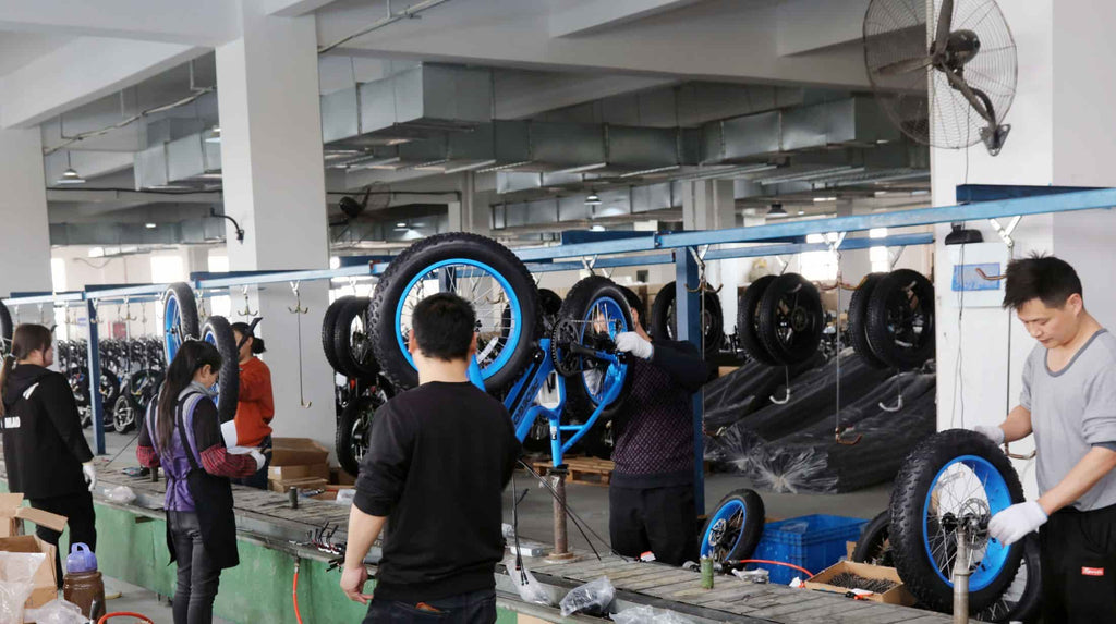 Workers on orderly DAMAXED production line assembling blue electric bicycles.