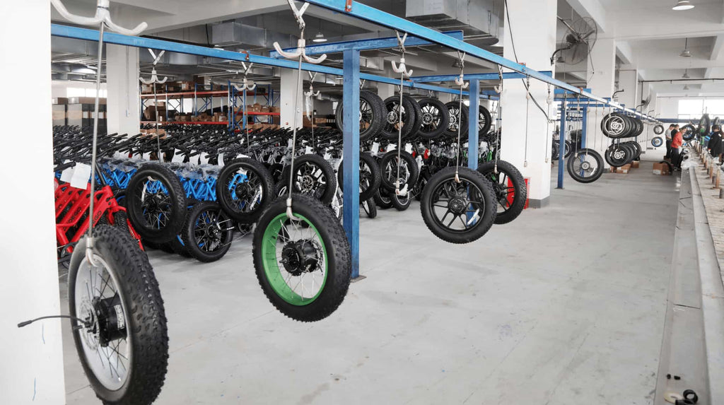 Tires waiting for assembly hang on production line, while neatly arranged assembled electric bikes sit in background.