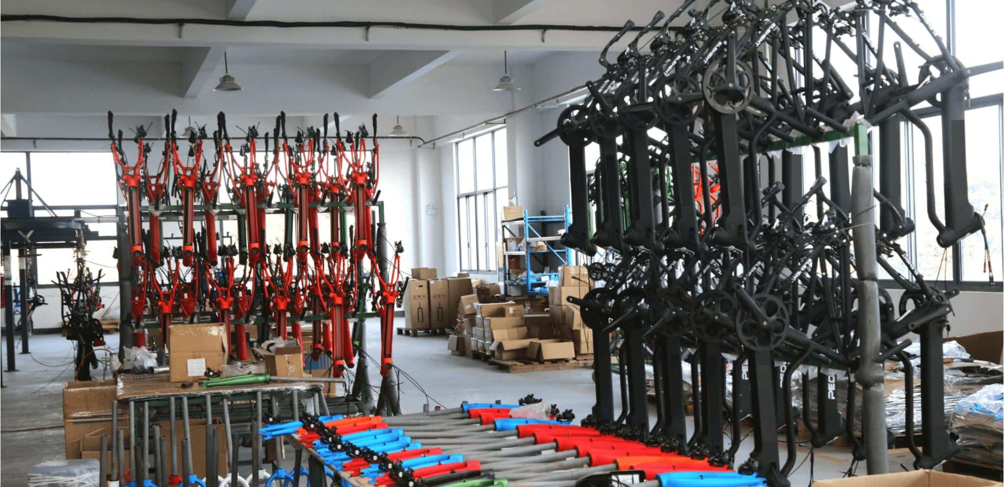 Freshly painted DAMAXED e-bike frames in red and black, along with some parts, are neatly displayed in a corner of the workshop, awaiting assembly.