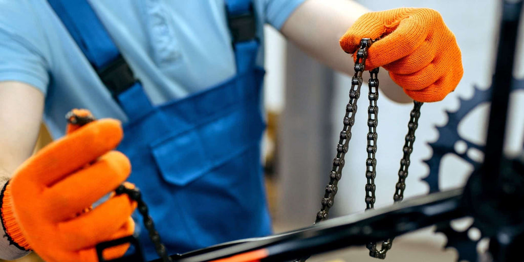 Engineer in blue overalls and orange gloves inspects electric bike chains.