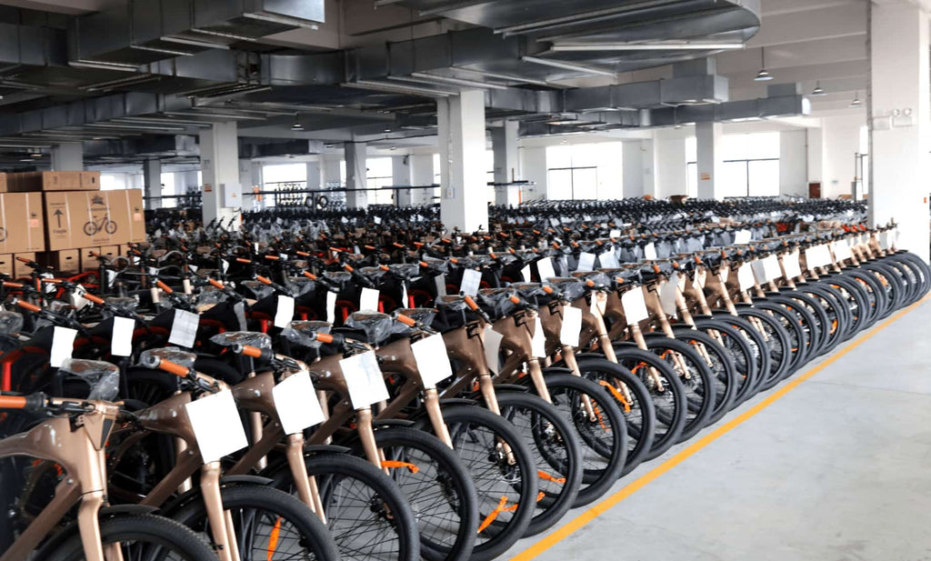 Electric bikes arranged neatly in DAMAXED warehouse, awaiting quality inspection, with packed finished products behind them.