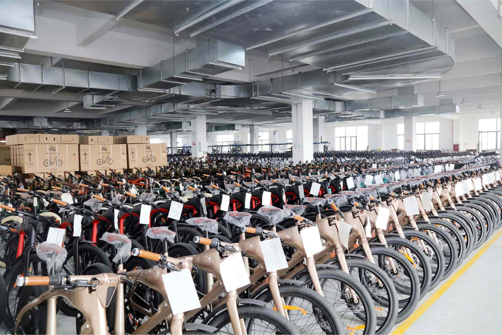 DAMAXED champagne e-bikes neatly displayed in spacious factory workshop with packed bikes in background for shipping.