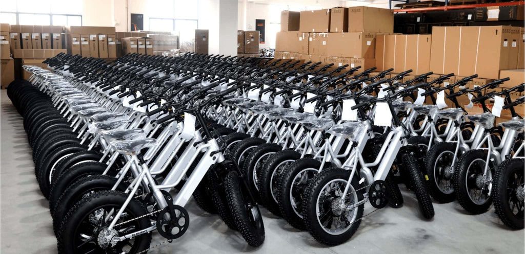 Rows of silver electric bikes are neatly arranged, waiting for quality inspection. Packed products surround them for transport.