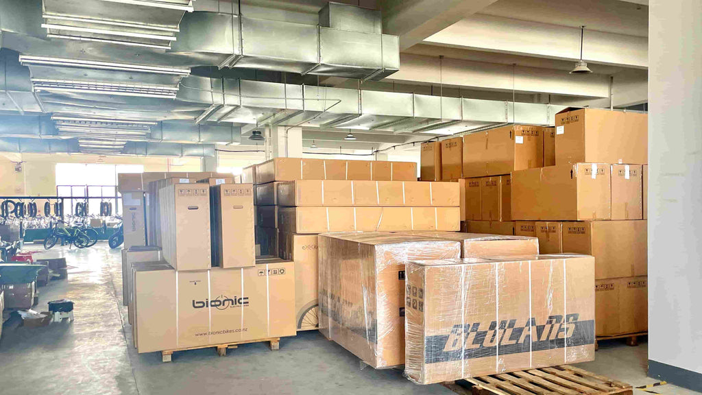 Packed DAMAXED e-bikes are neatly displayed in the warehouse, with some unassembled parts and bikes awaiting inspection.