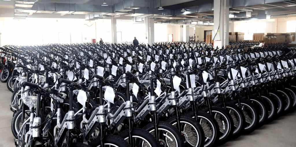 Rows of silver electric bikes neatly placed in factory warehouse, awaiting quality inspection.