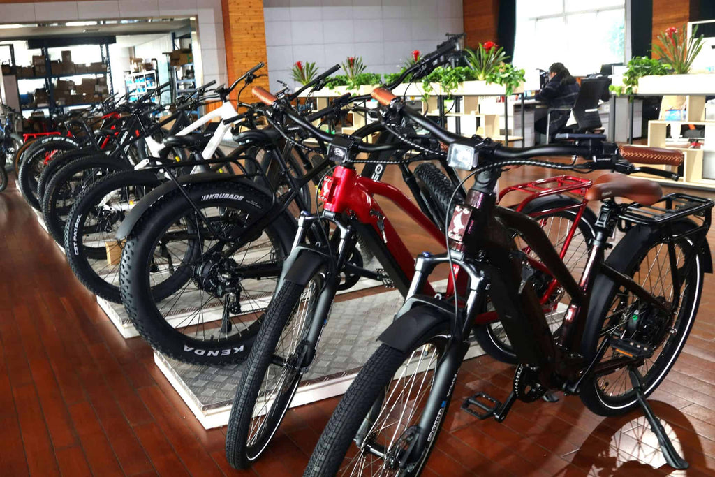 Corner of factory showroom displays 7-8 vertically arranged electric bikes in red, black, and white colors.