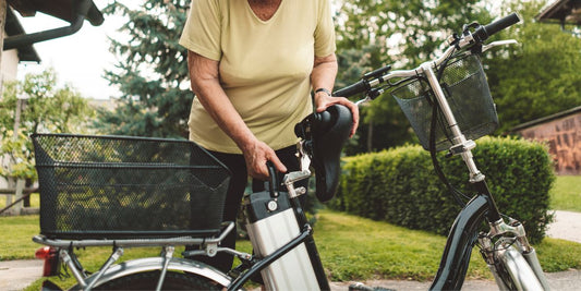 Middle-aged woman in a backyard with a green lawn, effortlessly removing the battery from the back of an electric bike by moving the seat.