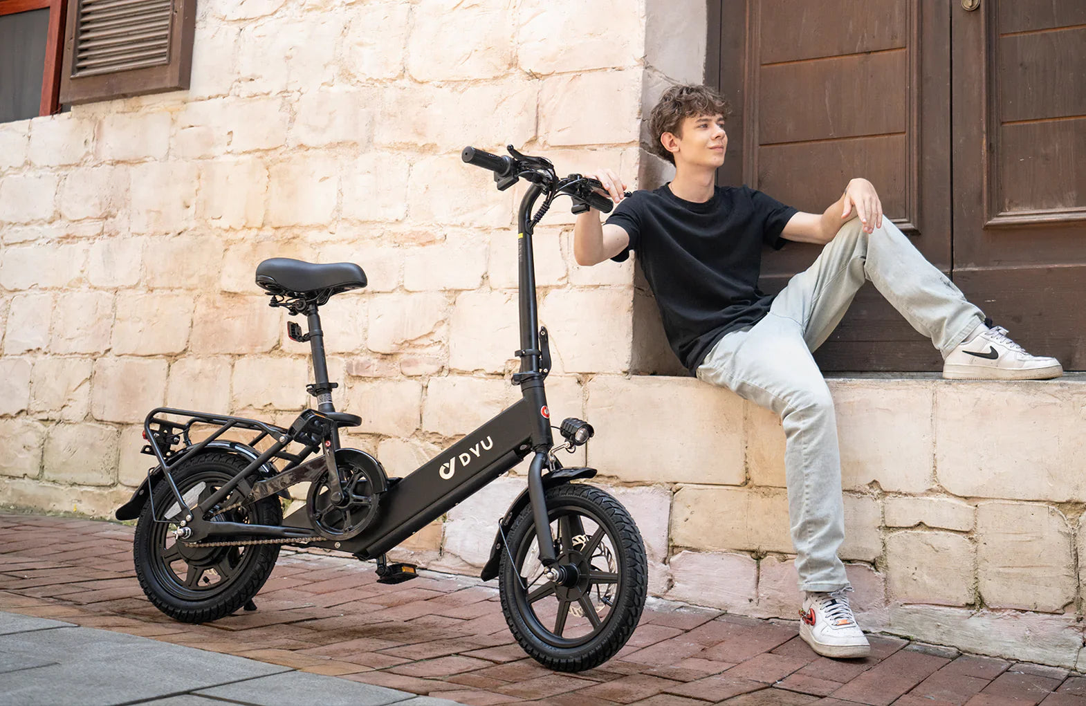 Person sitting next to a black C3 foldable electric bike on a stone step.
