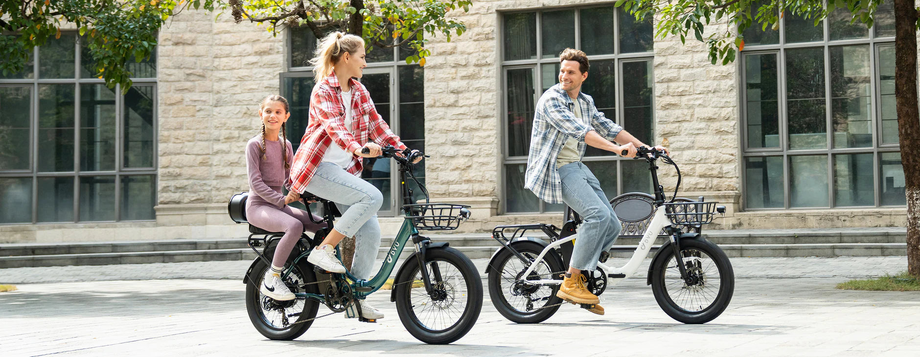Three people riding electric bikes on a sidewalk with a building in the background
