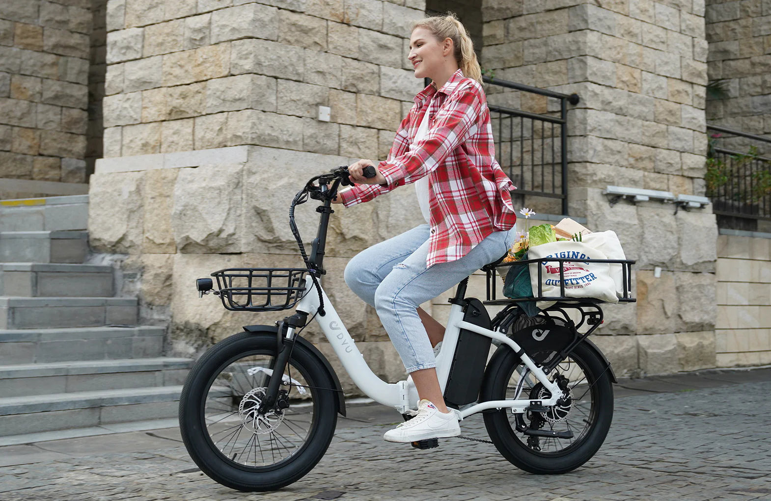 Woman riding a white DYU C9 electric bike with a basket in an urban setting