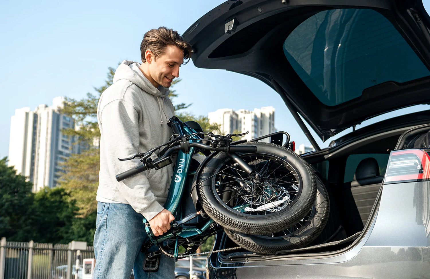 Man loading a folded DYU C9 electric bike  into the trunk of a car with cityscape in the background