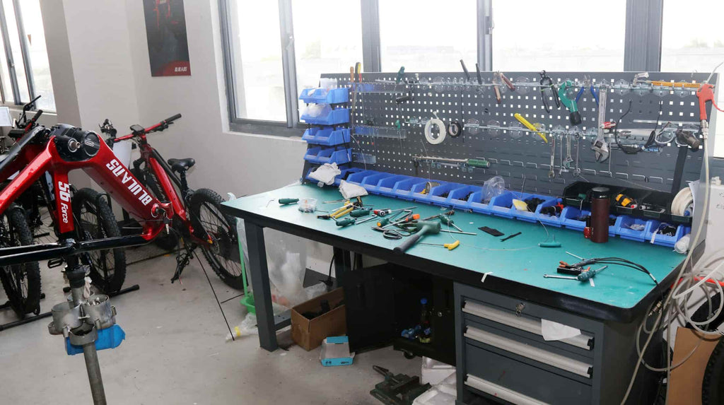 A red DAMAXED e-bike waits for fuction check next to a tool-filled operating table.